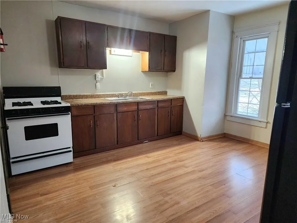 Kitchen with dark brown cabinets, white range with gas cooktop, light wood-type flooring, and freestanding refrigerator