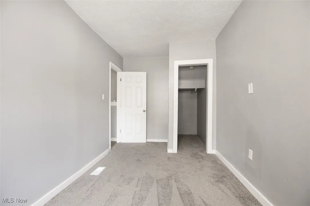 Unfurnished bedroom featuring light colored carpet, a textured ceiling, and a walk in closet