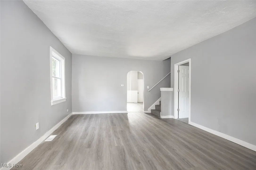 Empty room with arched walkways, light wood finished floors, stairs, and a textured ceiling