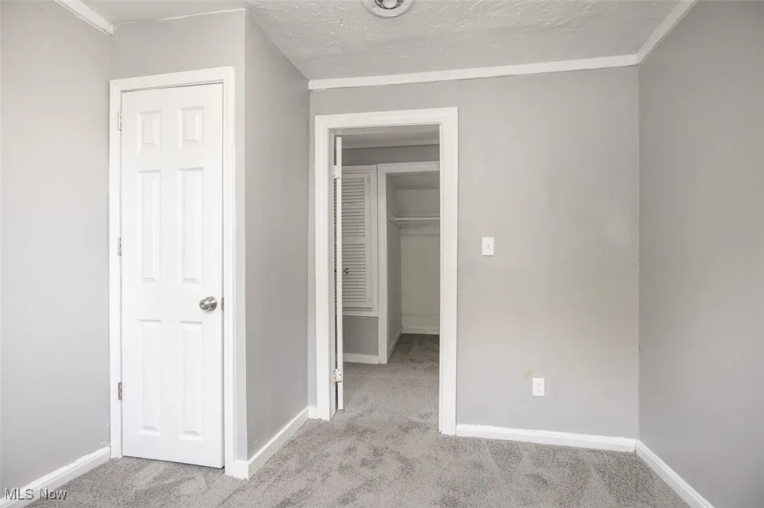 Unfurnished bedroom with a textured ceiling, light colored carpet, and a spacious closet