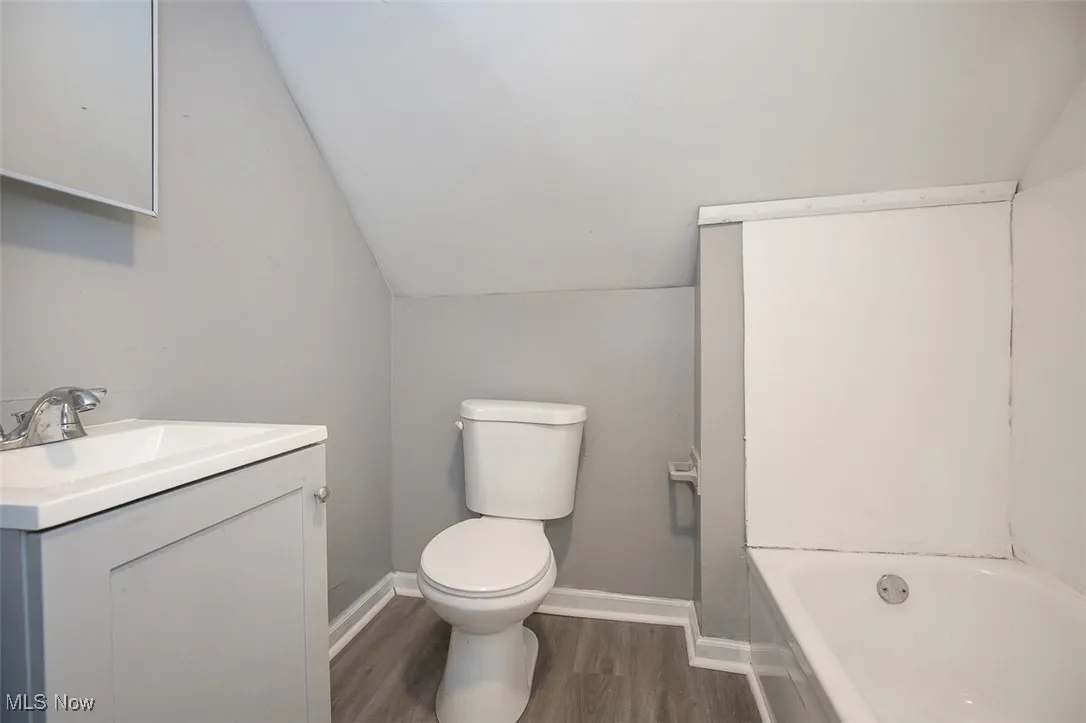 Full bath with lofted ceiling, a bathtub, dark wood-style floors, and vanity