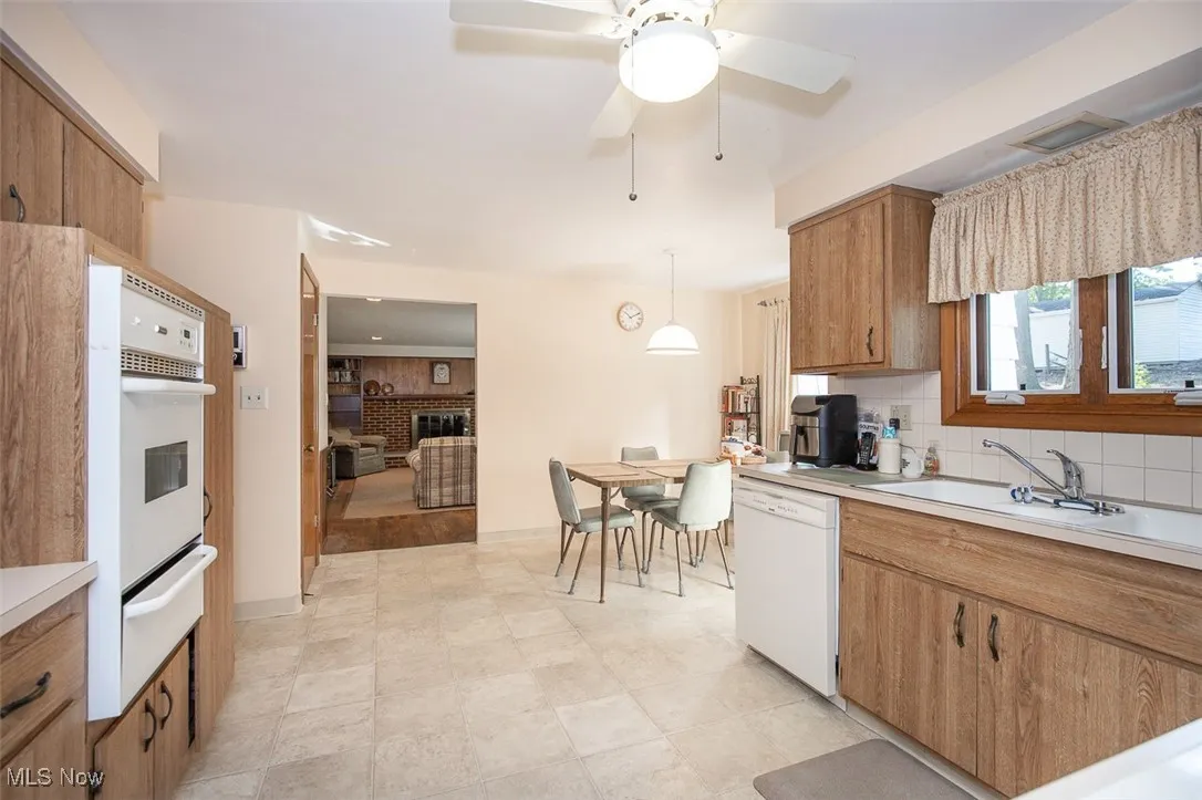 Kitchen with light countertops, brown cabinetry, backsplash, a warming drawer, and white appliances