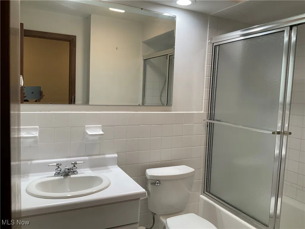 Bathroom featuring tile walls, vanity, and enclosed tub / shower combo