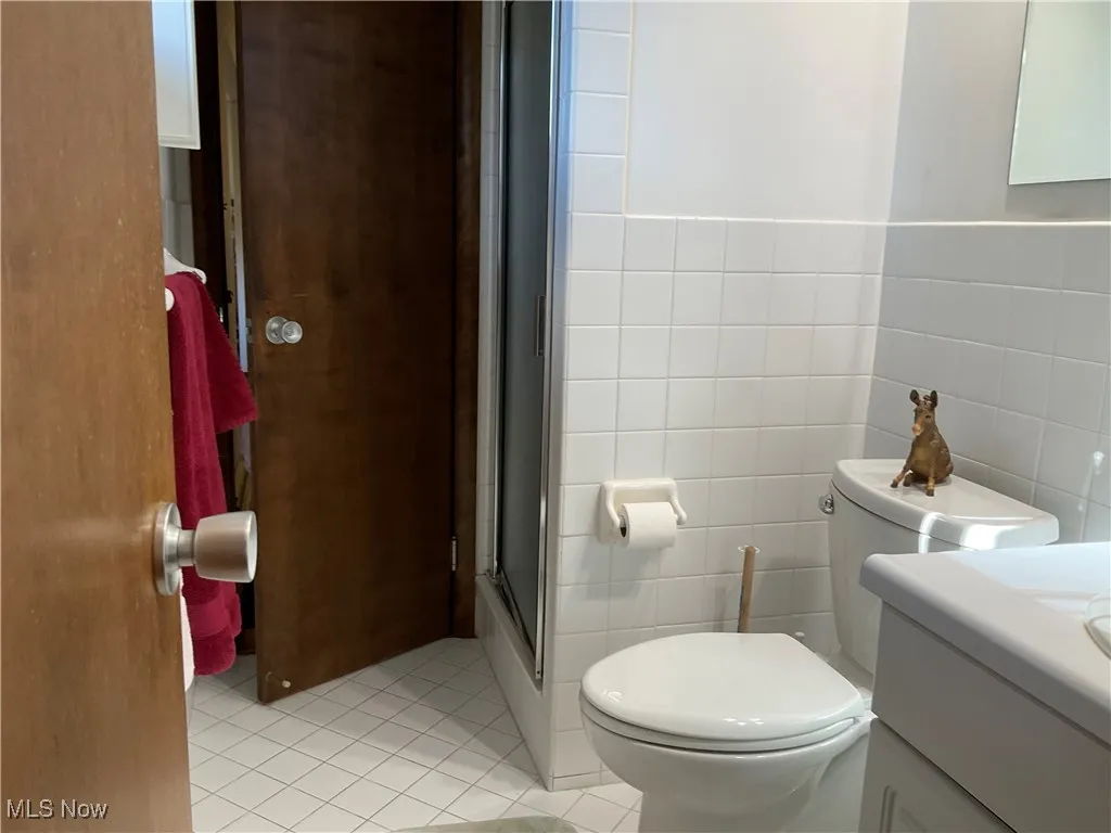 Full bathroom with light tile patterned flooring, tile walls, a stall shower, and vanity