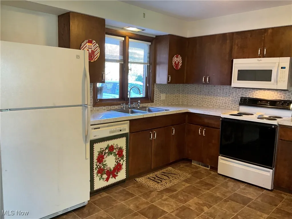 Kitchen with white appliances, light countertops, dark brown cabinetry, and tasteful backsplash