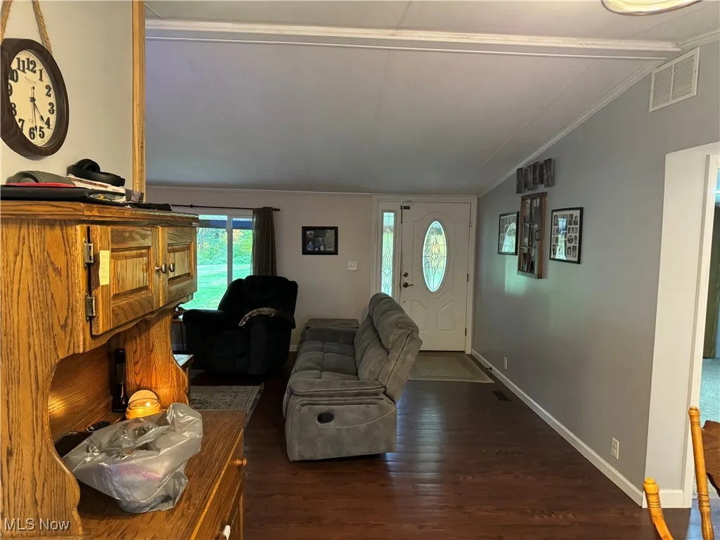 Entrance foyer with dark wood-type flooring, vaulted ceiling, and crown molding