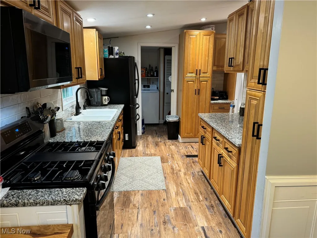 Kitchen featuring black appliances, backsplash, light stone countertops, light wood-style flooring, and brown cabinets