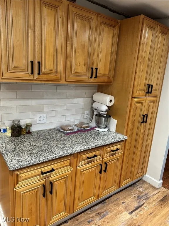 Kitchen with brown cabinetry, light stone countertops, light wood-type flooring, and backsplash
