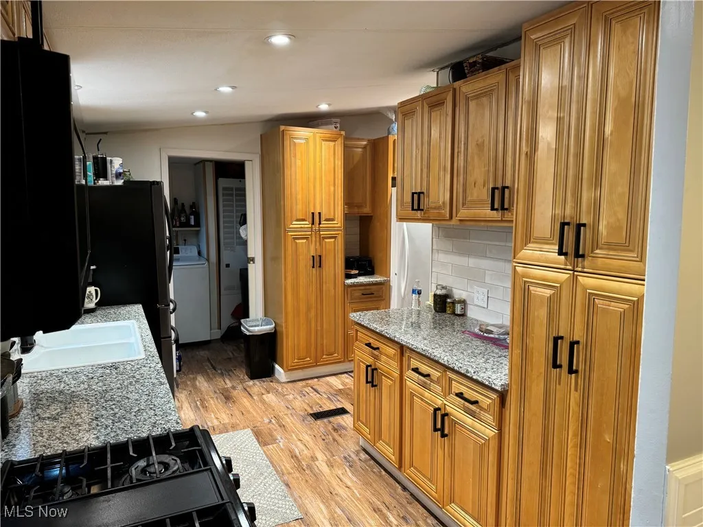 Kitchen with black range with gas cooktop, brown cabinets, light stone counters, backsplash, and light wood-type flooring