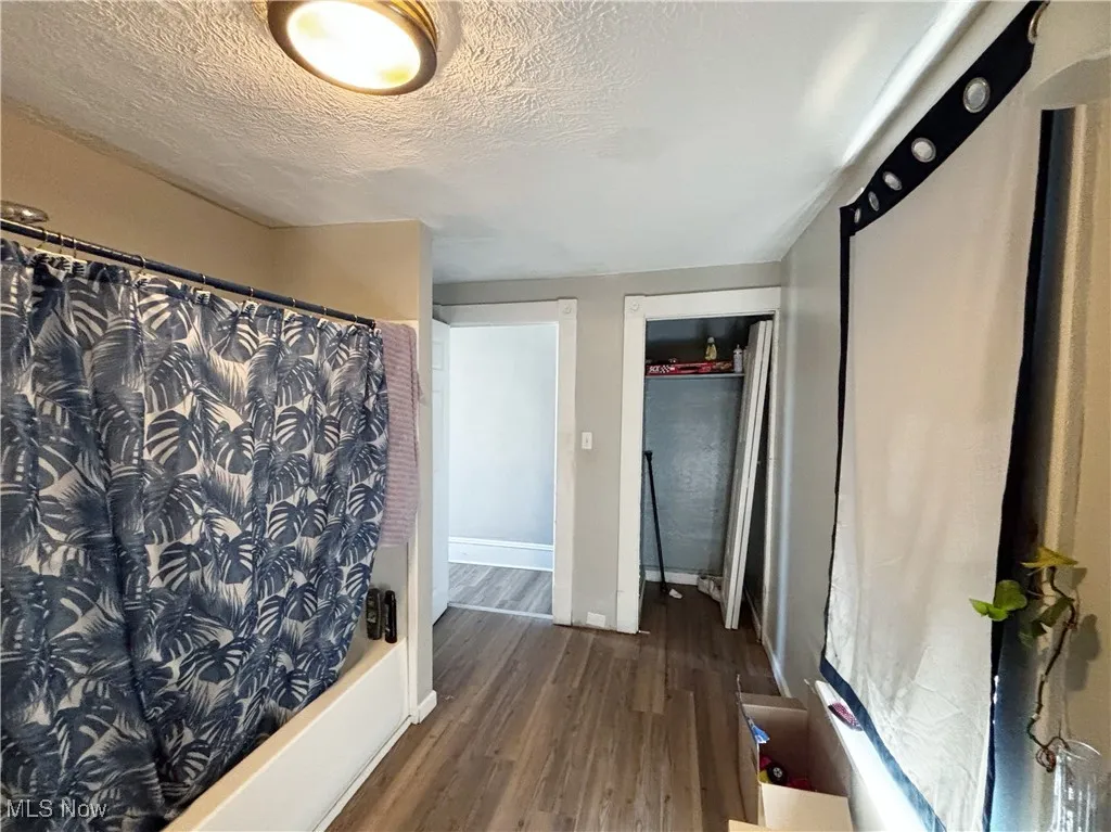 Bathroom with dark wood-type flooring, a textured ceiling, and shower / bath combo