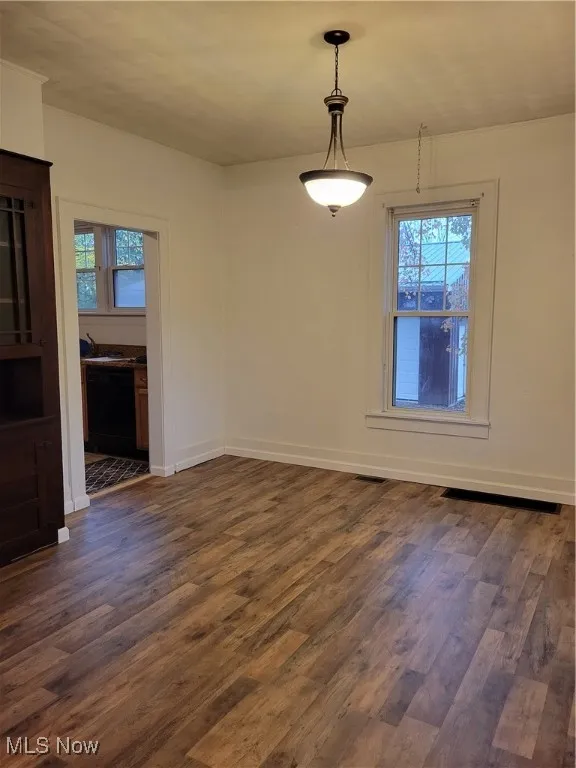 Unfurnished dining area with dark wood-style flooring and baseboards