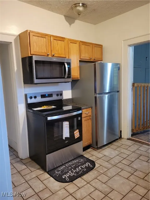 Kitchen featuring stainless steel appliances, dark countertops, a textured ceiling, and brown cabinetry