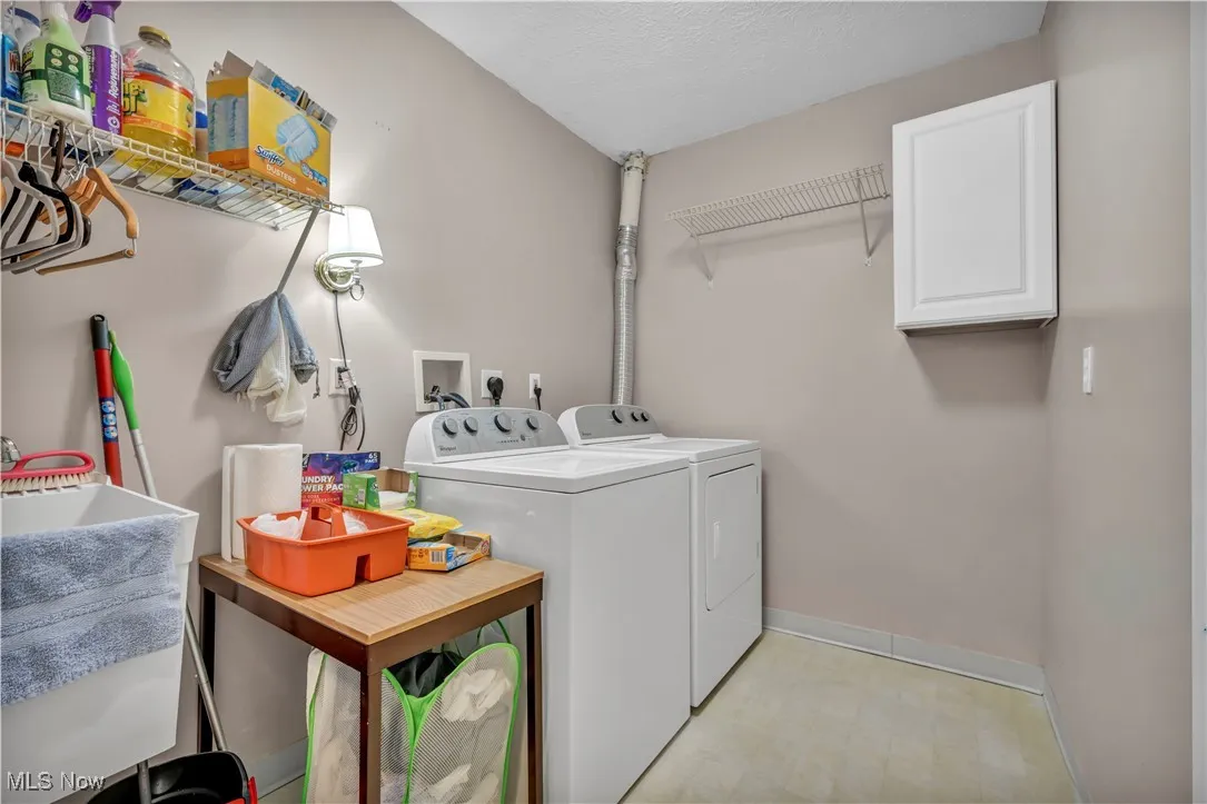 Washroom with separate washer and dryer, a textured ceiling, light flooring, and cabinet space