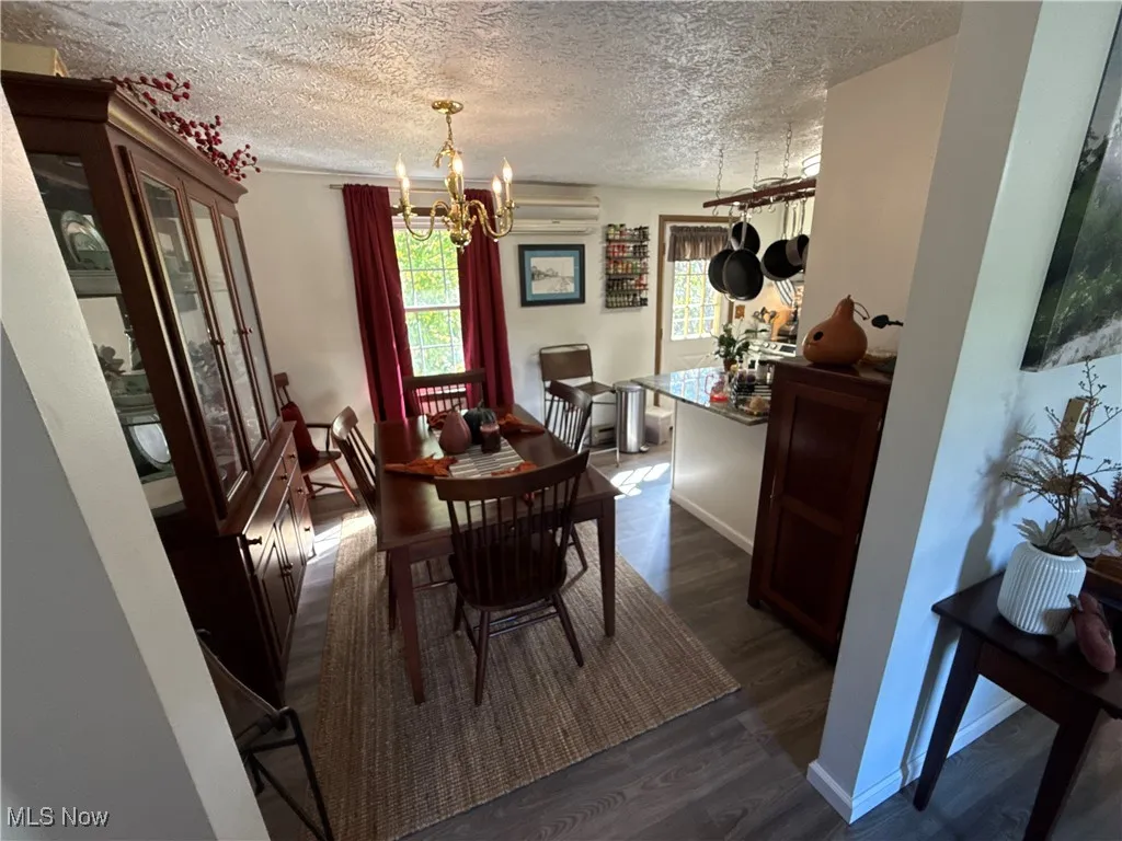 Dining area featuring dark wood-style floors, a chandelier, a textured ceiling, and an AC wall unit