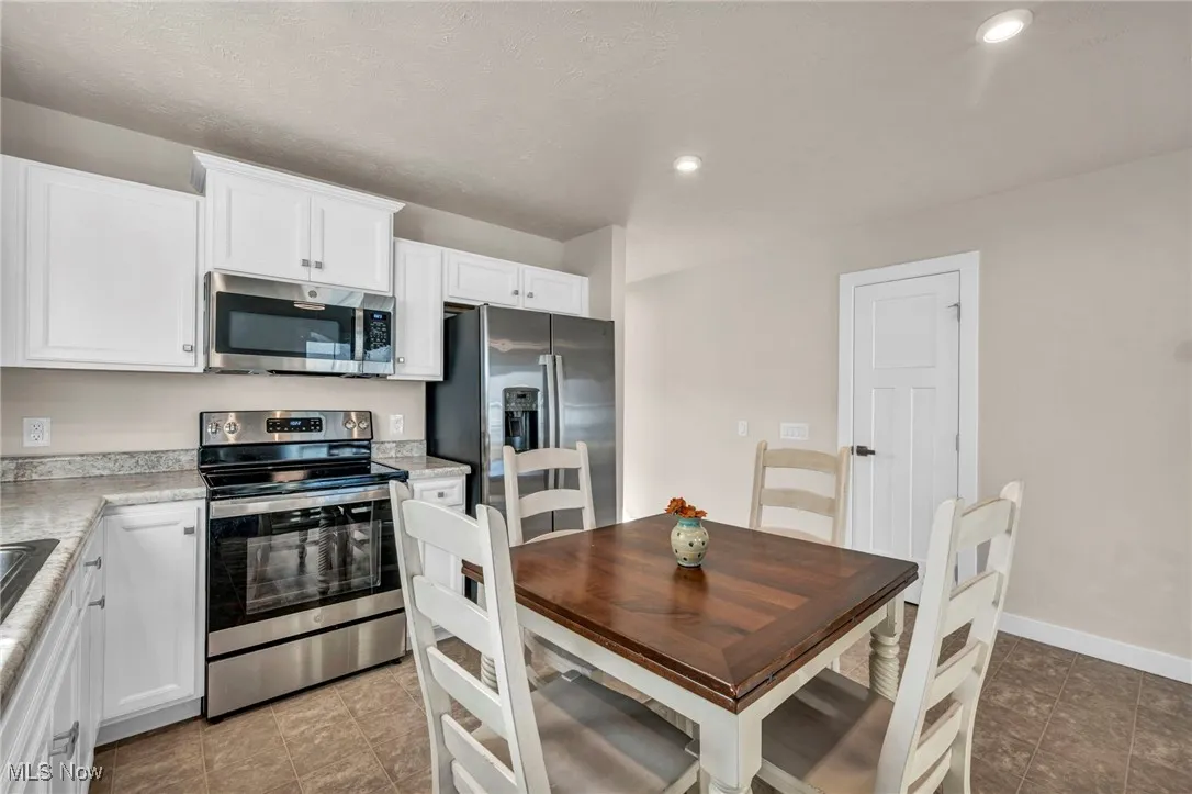 Kitchen with stainless steel appliances, light countertops, white cabinetry, recessed lighting, and dark tile patterned floors