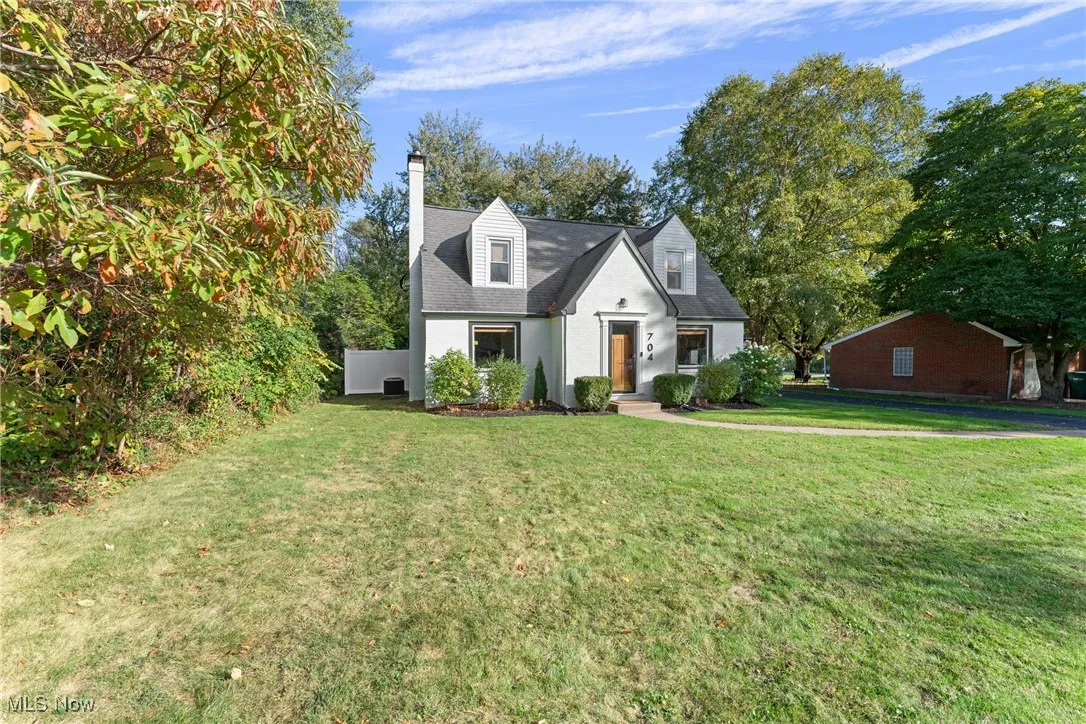 Cape cod-style house featuring a chimney and a front yard