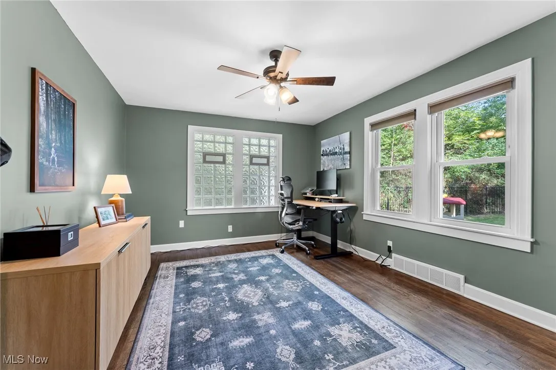 Office space with plenty of natural light, dark wood-style floors, and ceiling fan
