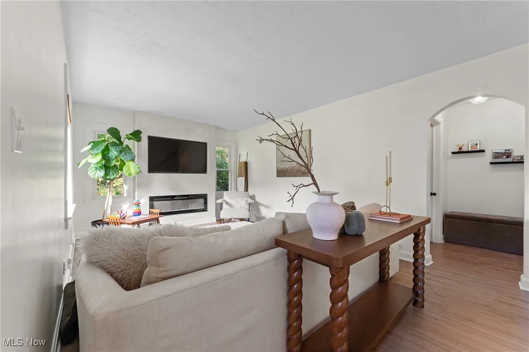 Living room with arched walkways, wood finished floors, and a glass covered fireplace