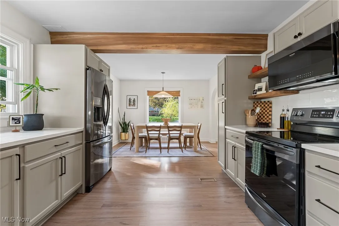 Kitchen with appliances with stainless steel finishes, light wood finished floors, tasteful backsplash, decorative light fixtures, and open shelves