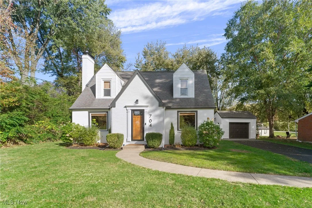 Cape cod home with a front yard, a chimney, brick siding, and a garage