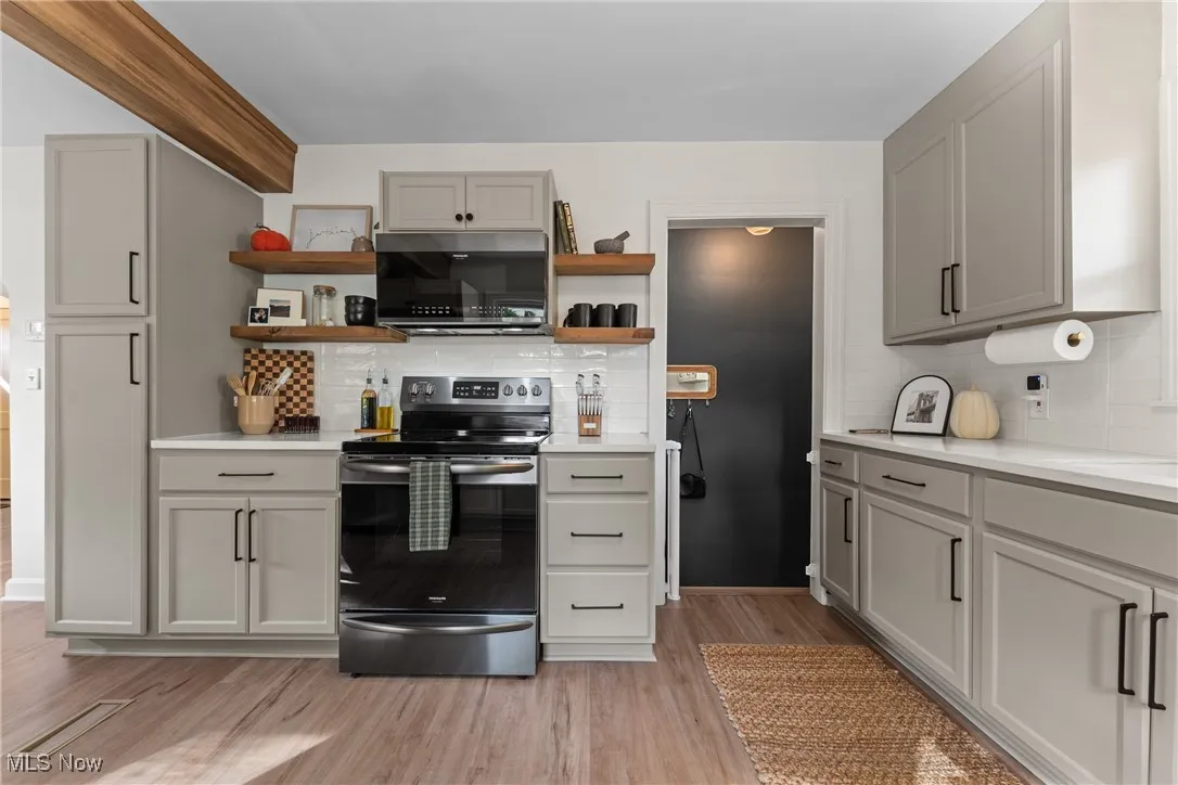 Kitchen featuring gray cabinetry, stainless steel appliances, tasteful backsplash, open shelves, and light wood-style flooring