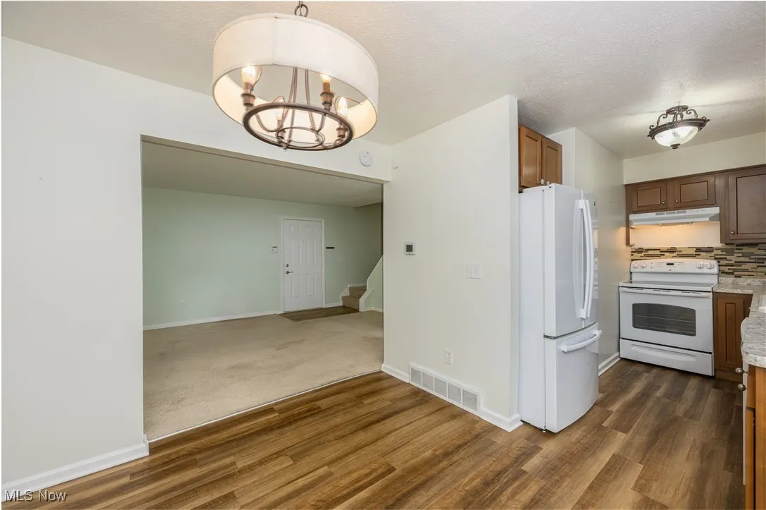 Kitchen featuring white appliances, decorative backsplash, dark wood-style floors, a textured ceiling, and pendant lighting