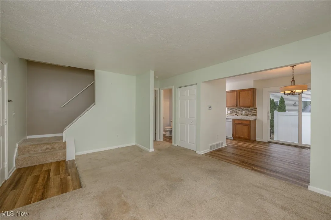 Unfurnished living room featuring light colored carpet, light wood-style flooring, a textured ceiling, and stairs