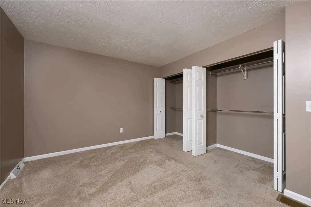 Unfurnished bedroom with a textured ceiling, light colored carpet, and a closet