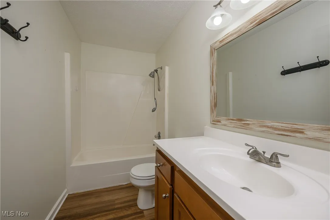 Bathroom with vanity, dark wood-type flooring, washtub / shower combination, and a textured ceiling