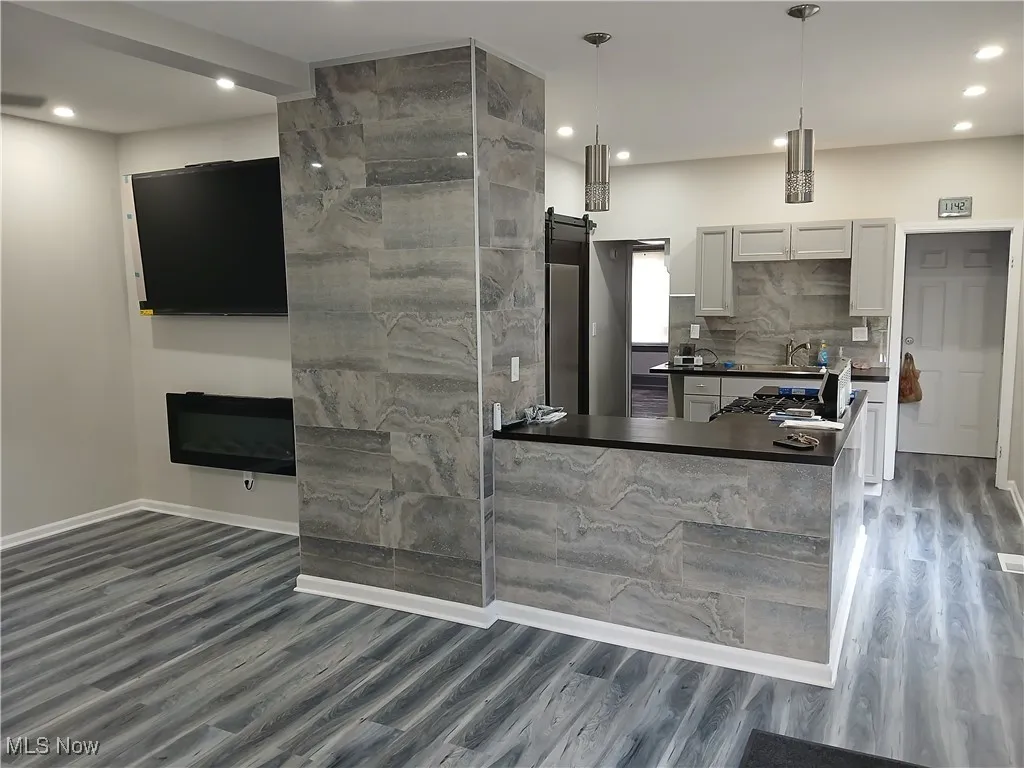 Kitchen with a barn door, dark countertops, backsplash, a peninsula, and dark wood-style floors
