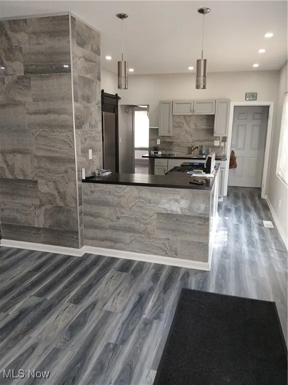 Living room with a barn door, decorative light fixtures, dark wood-style floors, a peninsula, and decorative backsplash