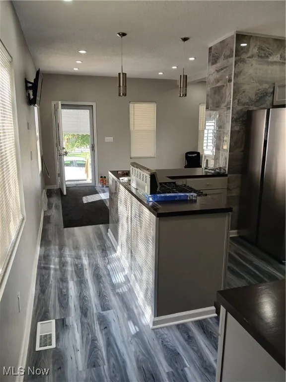 Kitchen featuring dark countertops, refrigerator, hanging light fixtures, dark wood finished floors, and recessed lighting