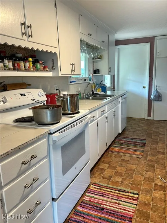 Kitchen with white cabinetry, white electric range oven, dishwasher, dark tile patterned flooring, and sink