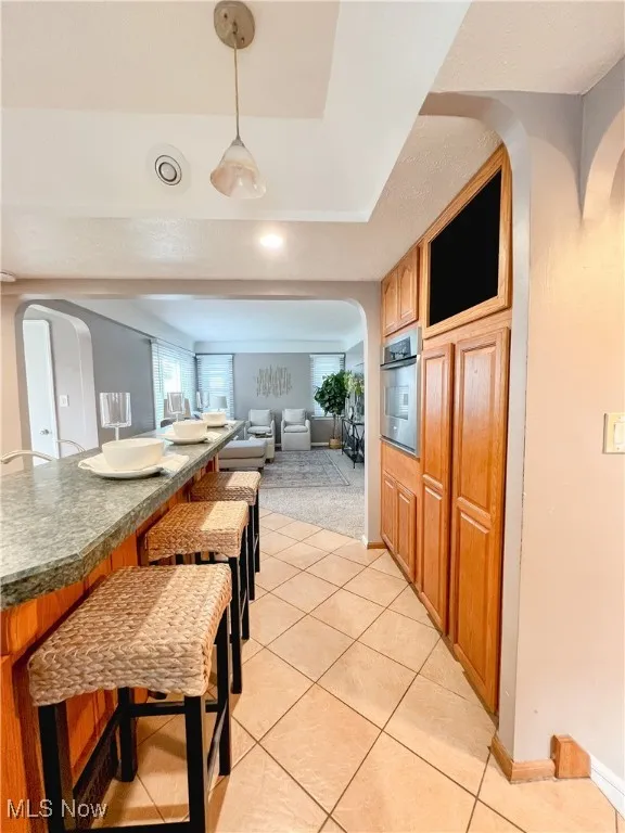 Kitchen with arched walkways, pendant lighting, a kitchen breakfast bar, light tile patterned floors, and open floor plan