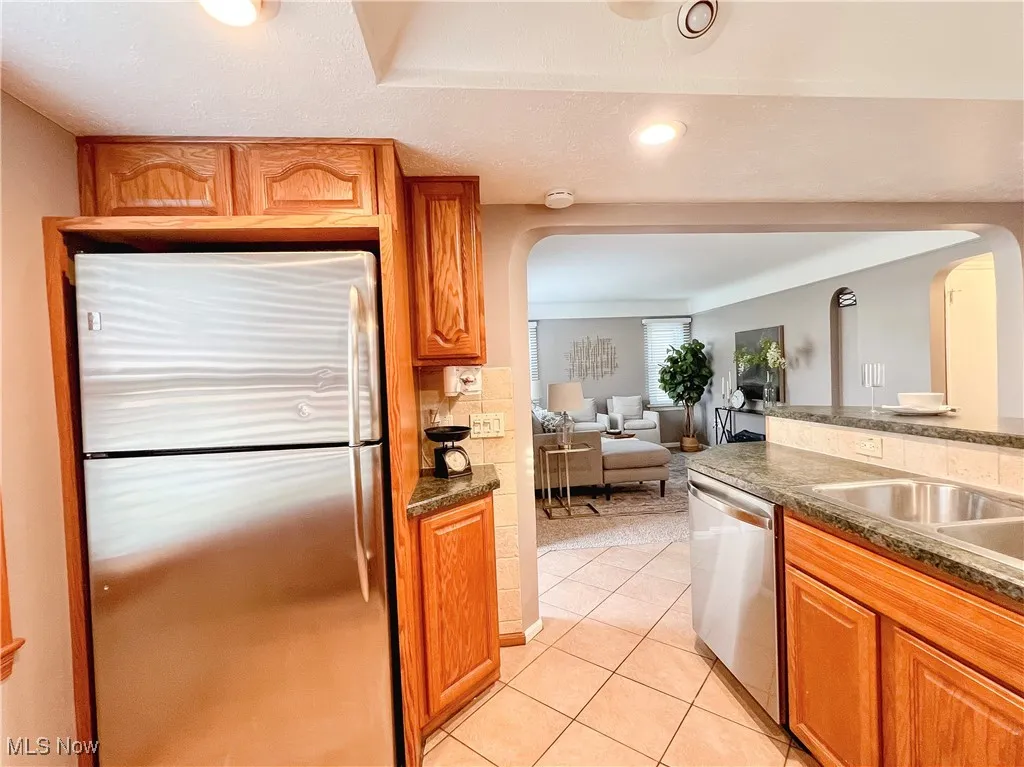 Kitchen featuring appliances with stainless steel finishes, arched walkways, light tile patterned floors, wood cabinetry, and recessed lighting