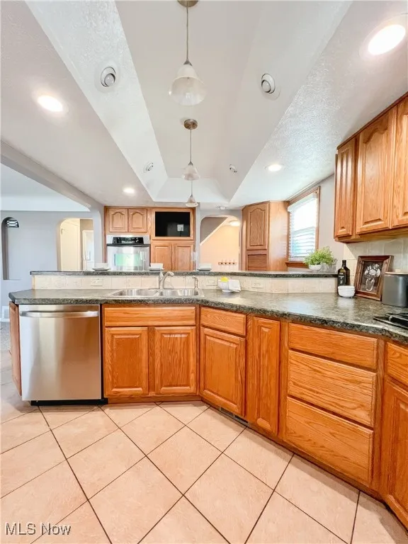 Kitchen featuring arched walkways, stainless steel appliances, light tile patterned floors, hanging light fixtures, and wood cabinets