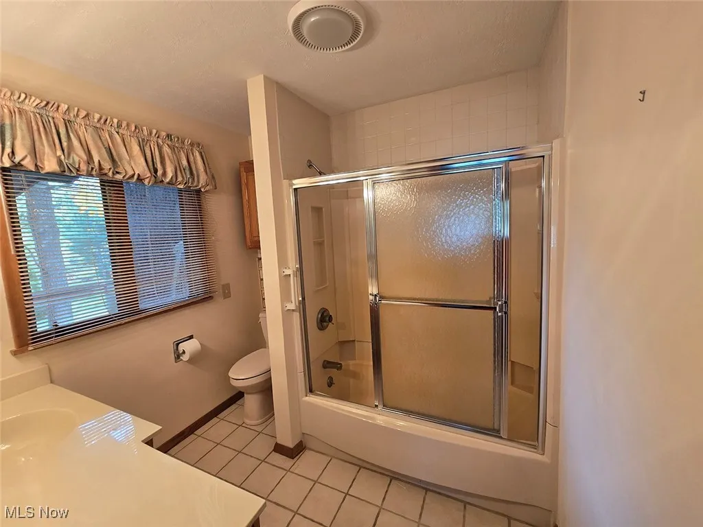 Full bathroom with vanity, light tile patterned flooring, enclosed tub / shower combo, and a textured ceiling