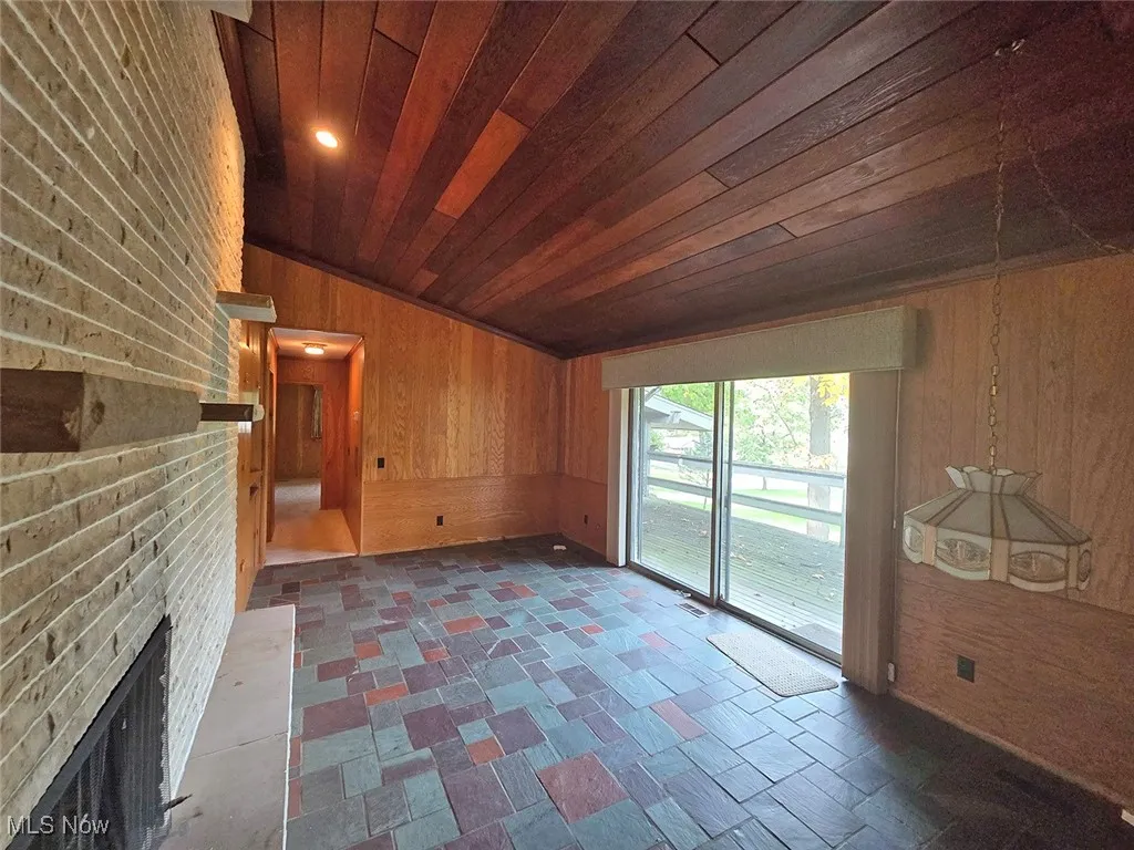 Unfurnished living room with wood walls, a fireplace, lofted ceiling, and wooden ceiling