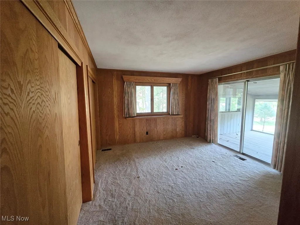 Unfurnished bedroom featuring access to outside, carpet flooring, wooden walls, and a textured ceiling