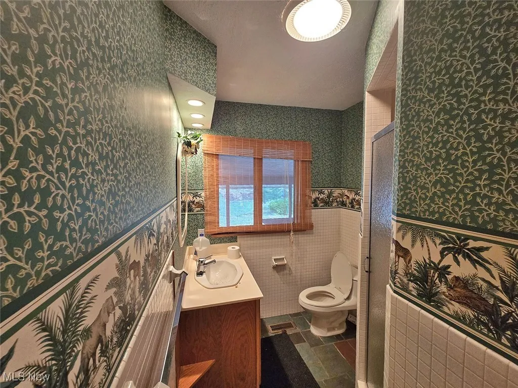 Bathroom featuring vanity, a stall shower, dark tile patterned flooring, wallpapered walls, and tile walls