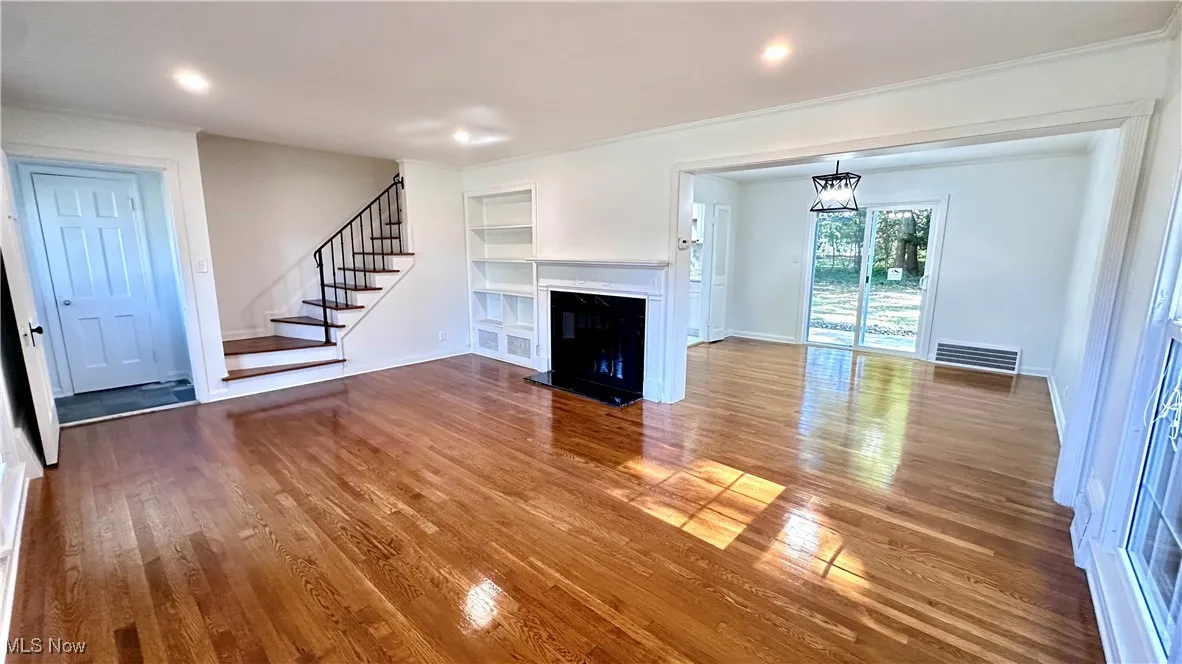 Unfurnished living room featuring built in shelves, a fireplace with raised hearth, wood finished floors, stairway, and recessed lighting