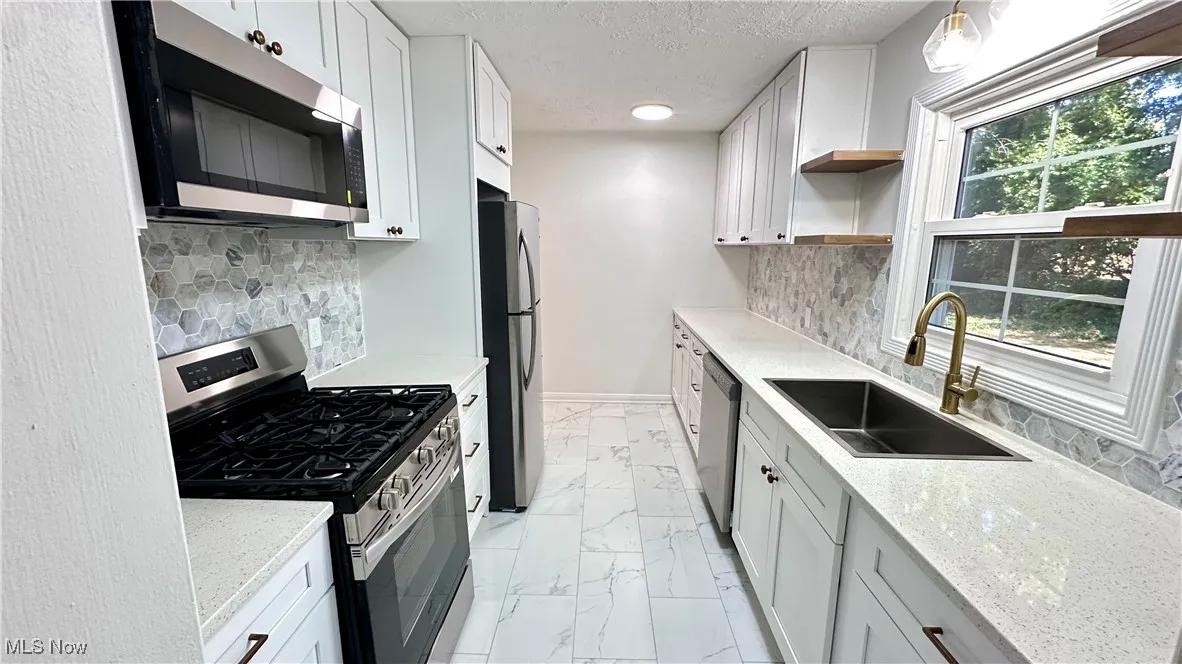 Kitchen featuring stainless steel appliances, open shelves, tasteful backsplash, light stone counters, and a textured ceiling