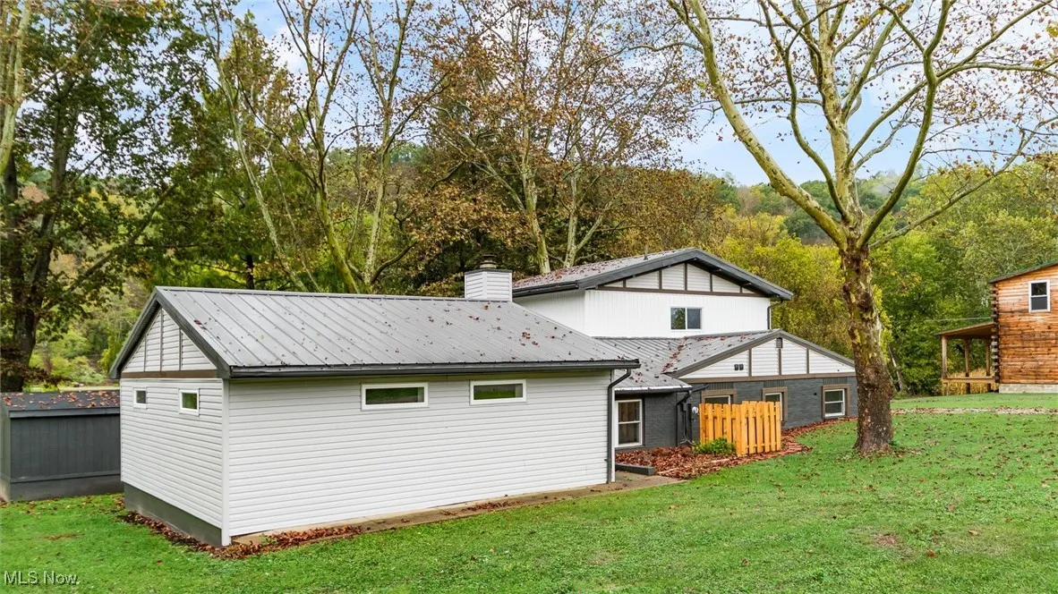Back of property featuring a lawn, a chimney, a metal roof, and view of scattered trees