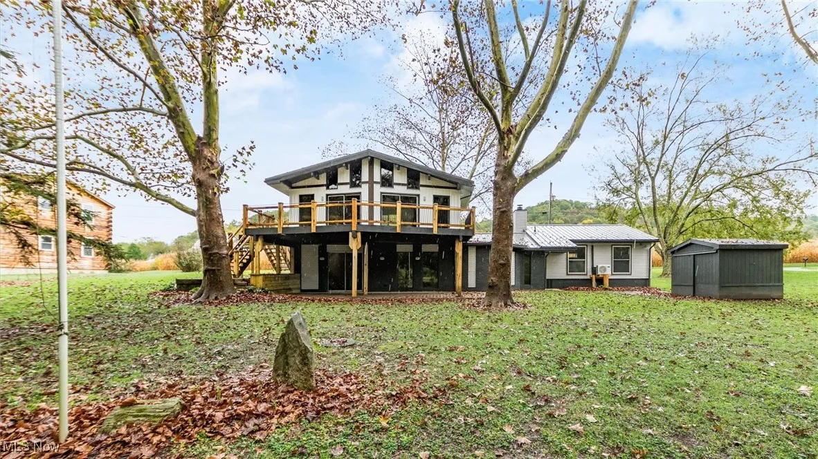 Rear view of property featuring stairway, a deck, a lawn, and a shed