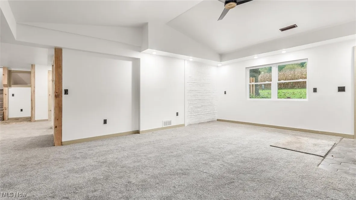 Empty room with vaulted ceiling, ceiling fan, and light colored carpet