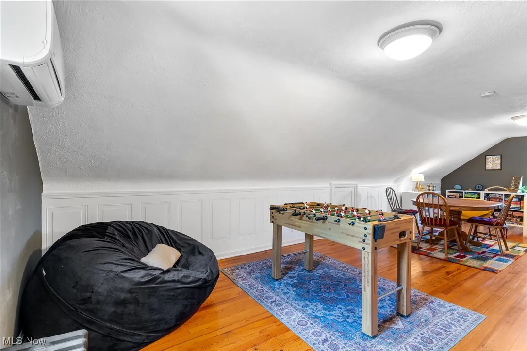 Playroom featuring hardwood / wood-style floors, a wall mounted AC, and vaulted ceiling