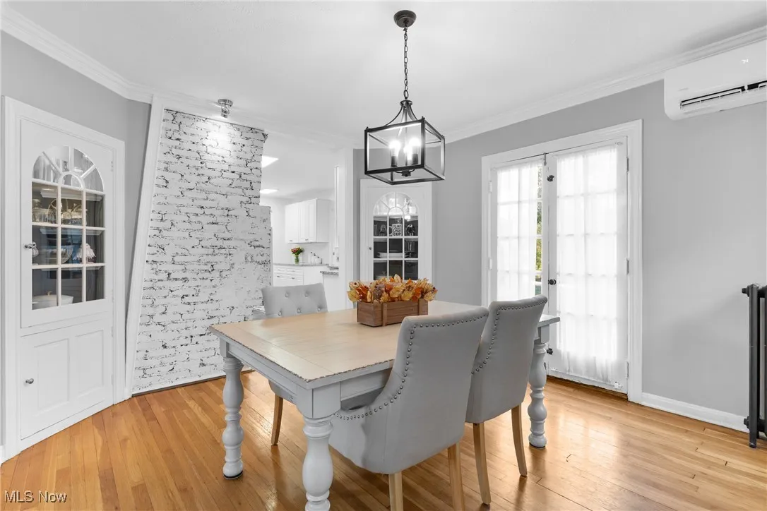 Dining room with light wood finished floors, a wall unit AC, crown molding, and a chandelier