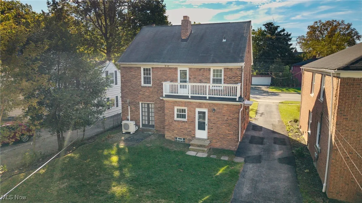 Rear view of property with brick siding, a chimney, a balcony, and entry steps
