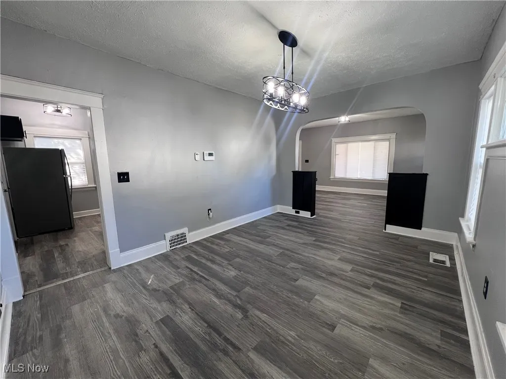Unfurnished dining area featuring arched walkways, a textured ceiling, dark wood-style flooring, and a chandelier