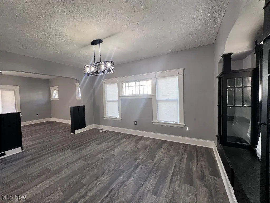 Unfurnished dining area featuring dark wood-style flooring, a textured ceiling, and arched walkways